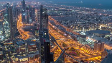 Dubai Şehir Merkezi gökdelenleri ve kavşağındaki trafiği gece gündüz gösteren fütüristik şehir manzarası. Gündoğumundan önce çatıdan modern kuleleri ve inşaatı olan sabah manzarası
