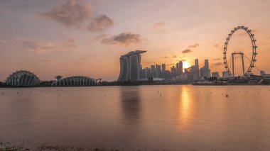 Singapur 'un şehir merkezindeki ufuk çizgisinde gün batımı, Doğu Bahçe zaman çizgisinin karşısından izleniyor. Gökdelenlerin arkasındaki güneş. Singapur. Sudaki yansıma