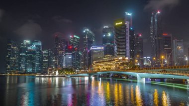 Esplanade Köprüsü ve şehir merkezindeki gökdelenler arka planda Singapur 'da gece vakti hızlandırılmış. Aydınlatılmış kuleler suya yansıyor
