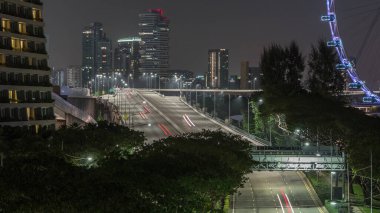 Singapur 'un marina körfezi bölgesinde bir cadde ve köprü üzerinde arabalarla trafik vardı. Arka planda gökdelenler vardı.