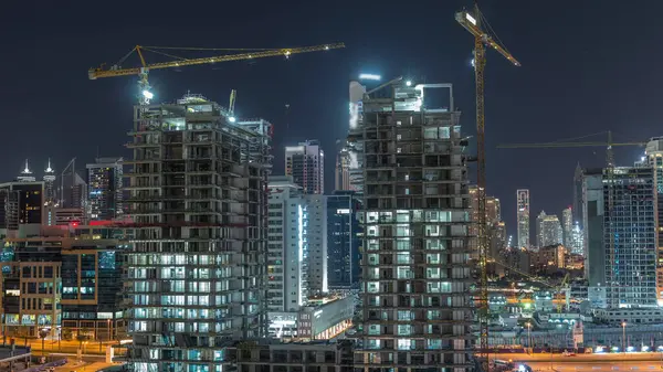 İnşaat halindeki gökdelenlerin hava görüntüsü Dubai 'de gece vakti büyük vinçlerle. Arka planda şehir merkezi olan bir işletme alanı. Birleşik Arap Emirlikleri