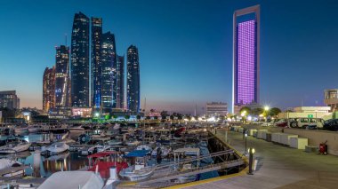 Al Bateen marinası Abu Dabi, gün batımından gün batımına kadar. Limanda tekneler ve arka planda aydınlatmalı modern gökdelenler.