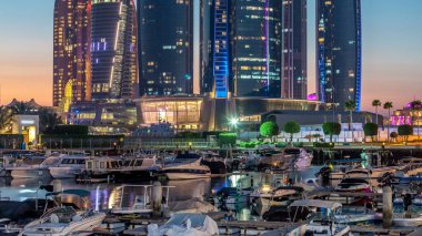 Al Bateen marinası Abu Dabi gündüz, gün batımından sonra tekneler ve yatlarla aydınlatılmış modern gökdelenler arka planda.