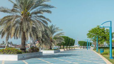 Abu Dabi 'deki sahil şeridi boyunca uzanan Corniche Bulvarı plajı parkında arka planda gökdelenler var. Avuçlar yana. Güneşli bir günde mavi gökyüzü