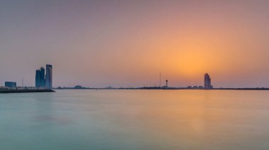 Abu Dabi 'de günbatımı Marina Adası üzerinde, Corniche manzaralı. Turuncu sıcak ışık ve suyun yansıması
