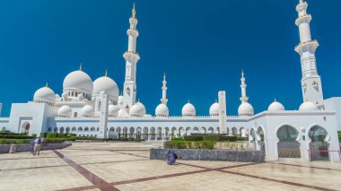 Birleşik Arap Emirlikleri 'nin başkenti Abu Dabi' deki Şeyh Zayed Büyük Camii zaman atlaması. Kubbeler ve minarelerle yan manzara. Ön planda çalılıklar. Güneşli bir günde mavi gökyüzü