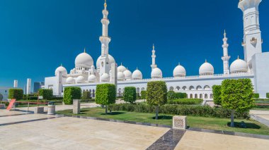 Birleşik Arap Emirlikleri 'nin başkenti Abu Dabi' deki Şeyh Zayed Büyük Camii zaman atlaması. Kubbeler ve minarelerle yan manzara. Ön planda ağaçlar. Güneşli bir günde mavi gökyüzü
