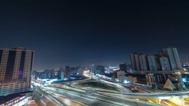 Panorama, Ajman hava sahasında büyük bir kavşakta trafiği gösteriyor. Gece vakti çatıdan görünüyor. Birleşik Arap Emirlikleri 'nde üst geçitle kesişen birçok araba var. Arkaplanda gökdelenler