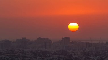 Ajman 'da gün batımı, çatıdaki zaman ayarlı hava manzarası. Birleşik Arap Emirlikleri 'nde turuncu gökyüzünde büyük güneşin akşam manzarası.