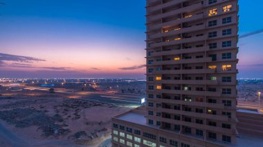 Ajman 'da çatıdan gece kuleye kule ve kavşakta trafik olan şehir manzarası. Birleşik Arap Emirlikleri 'nde gün batımından sonra aydınlanan binaların hava manzarası.