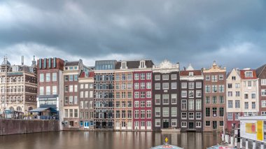 Damrak 'taki renkli Kanal Evleri' nin gece ışığında aşırı hızlanması dramatik bulutların altında geçen teknelerle suya yansıdı. Hollanda, Amsterdam 'ın büyüleyici manzarası