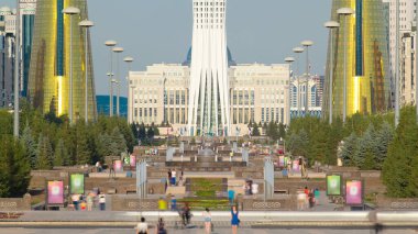 Astana, insanlar güneşli bir günde şehrin arka planında Baiterek bölgesinin başkanlık sarayının sembolü olan çeşmelerle yürüyüp rahatlıyorlar. Nur-Sultan şehri, Kazakistan
