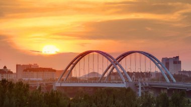 Köprünün üzerinde gün batımı zamanı geçiyor. Arkaplanda bulutlar ve ulaşım trafiği var. Şehir silüeti. Orta Asya, Nur-Sultan şehri, Kazakistan