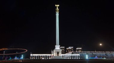 Stele anıtı Kazak Eli ve kuş Samruk geceleri ve Bağımsızlık Sarayı hiperhız ve trafik ön planda. Nur-Sultan şehri, Kazakistan