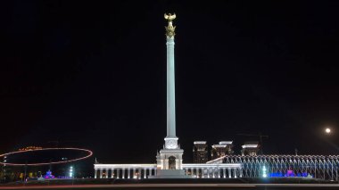 Stele anıtı Kazak Eli ve kuş Samruk geceleri ve Bağımsızlık Sarayı hiperhız ve trafik ön planda. Nur-Sultan şehri, Kazakistan