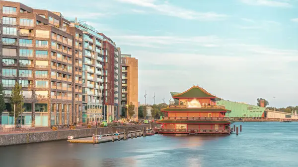 Sudaki pagoda şeklinde bir Çin restoranının hipervanesi, tarihi şehir merkezi binalarının ve günbatımında modern mimarinin arka planına karşı kurulur. Amsterdam, Hollanda