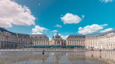 Place de la Bourse ve Miroir d 'eau hiperlapse Bordeaux, Fransa' da, tarihi mimariyi yansıtıyor. Turistler şehir simgesi ve çeşmenin tadını çıkarıyorlar. Trafik ve tramvay zamanı geçiyor..