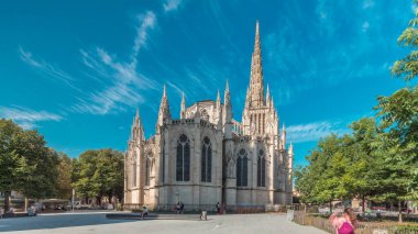 Saint-Andre de Bordeaux Katedrali. Mavi gökyüzünün altında ikiz kuleleri olan hızlandırılmış zaman atlaması. Yeşil ağaçlar ve meydanda yürüyen insanlar sakin bir şehir atmosferi yaratıyor. Bordeaux, Fransa