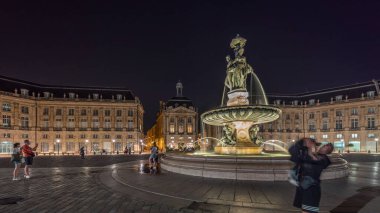 Panorama, Place de la Bourse 'u ve Fransa' nın Bordeaux şehrindeki çeşmeleri gösteriyor. Aydınlatılmış tarihi binalar büyük meydanın sınırında. Trafik ve sokakta hareket sahneyi güçlendirir