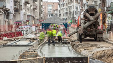 Beton döşeme, yol onarım şantiyesinde birçok işçi ve mikser zaman ayarlarıyla çalışıyor. Tramvay raylarının yeniden inşası