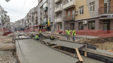 Beton döşeme, yol onarım şantiyesinde metal takviyesinde birçok işçi ve mikser zaman ayarlı olarak çalışır. Tramvay raylarının yeniden inşası