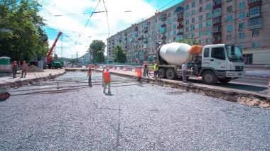 Tramvay rayları onarımı ve bakım zamanı olan bir yol inşaatı. Somut, kavşağın ortasında turuncu mikserle çalışıyor. Yeni toplu taşıma için demiryolu raylarının değiştirilmesi