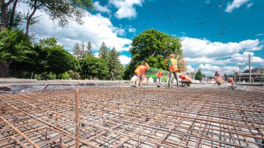 Tramvay rayları onarılan ve bakım süreleri yüksek olan yol inşaatı. Metal bir şebekeye beton dökülüyor. Birçok işçiyle kavşağın ortası.