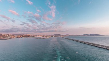 Gün batımında açık denizde yelken açan gemiden dalgalı ve limanlı deniz manzarası. Marsilya kıyısı, Fransa