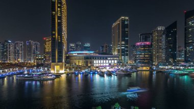 Dubai Marina 'nın hava görüntüsü, alışveriş merkezi, restoranlar, kuleler ve yatlar, Birleşik Arap Emirlikleri. Aydınlatılmış binalar ve liman manzaralı bir kanal.