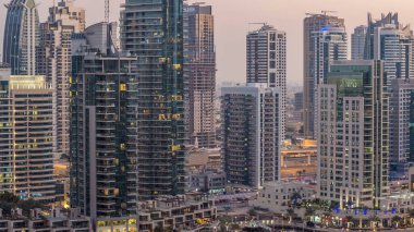 Lüks Dubai Marina Kanalı 'ndan geçen tekneler ve gece gündüz restoranlarla gezinti günbatımından sonra aydınlık gökdelenlerle yukarıdan manzaralı. Dubai, Birleşik Arap Emirlikleri