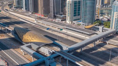 Futuristik binada Dubai metro ve tramvay istasyonu ve lüks gökdelenler arkasında timelapse içinde Dubai Marina, Birleşik Arap Emirlikleri. Hava üst görünümden Jlt trafik ile Şeyh zayed yolu üzerinde