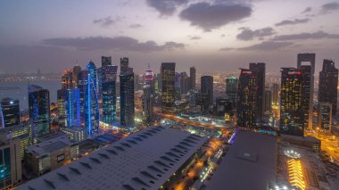 Batı Körfezi bölgesinin ufuk çizgisi Doha 'da günden geceye geçiş zamanı, Katar. Günbatımından sonra modern gökdelenlerin çatıdan görünüşü aydınlandı. Yolda trafik vardı.