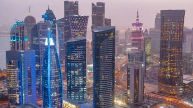 Batı Körfezi bölgesinin ufuk çizgisi Doha 'da günden geceye geçiş zamanı, Katar. Günbatımından sonra modern gökdelenlerin çatıdan görünüşü aydınlandı. Yolda trafik vardı.