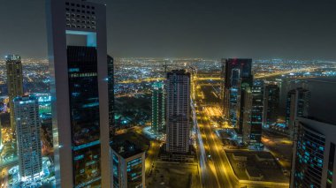 Katar 'ın Doha Zaman Çizelgesi' nde Batı Körfezi bölgesinin ufuk çizgisi. Aydınlatılmış modern gökdelenler geceleri çatıdan gökyüzü manzarası. Yolda trafik vardı.