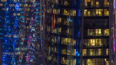 İçerideki cam ve çelik ofis aydınlatması ve çalışan insanların çok katlı binasının zaman çizelgesi. Gökdelenlerin gece aydınlanması. Doha, Katar