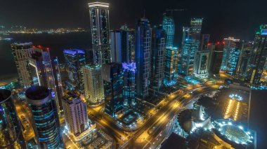 Katar 'ın Doha Zaman Çizelgesi' nde Batı Körfezi bölgesinin ufuk çizgisi. Aydınlatılmış modern gökdelenler geceleri çatıdan gökyüzü manzarası. Yolda trafik vardı.