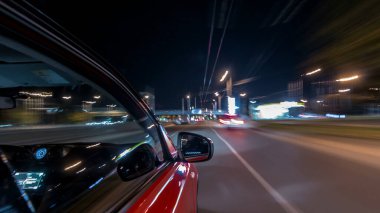 Hızlı arabanın yanından gelen bir drivelapse, gece caddesinde hızla ilerliyor. Işıklar yüksek hızda arabayı yansıtıyor. Modern bir şehrin hızlı ritmi. Bulanık hareket