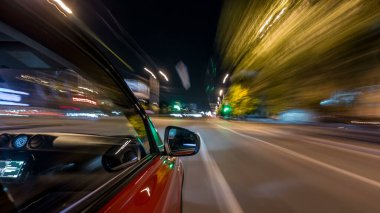 Hızlı arabanın yanından gelen bir drivelapse, gece caddesinde hızla ilerliyor. Işıklar yüksek hızda arabayı yansıtıyor. Modern bir şehrin hızlı ritmi. Bulanık hareket