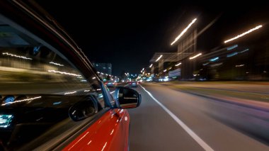 Hızlı arabanın yanından gelen bir drivelapse, gece caddesinde hızla ilerliyor. Işıklar yüksek hızda arabayı yansıtıyor. Modern bir şehrin hızlı ritmi. Bulanık hareket