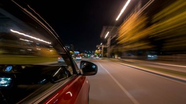 Hızlı arabanın yanından gelen bir drivelapse, gece caddesinde hızla ilerliyor. Işıklar yüksek hızda arabayı yansıtıyor. Modern bir şehrin hızlı ritmi. Bulanık hareket