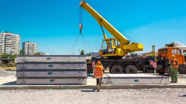 Yol inşaatı zamanında sarı vinçle beton plakaları boşaltıyorum. Şapkalı ve üniformalı endüstriyel işçiler. Şehir caddesindeki tramvay raylarının yeniden inşası