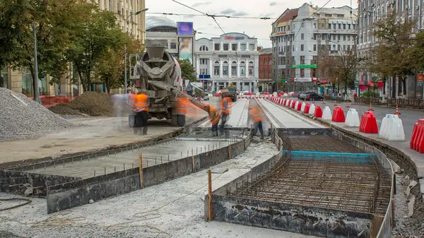 Beton, turuncu üniformalı ve mikser makineli birçok işçiyle yol inşaatı için özel plakaların yanında çalışıyor. Tramvay raylarının yeniden inşası