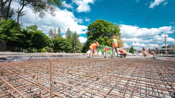 Tramvay rayları onarılan ve bakım süreleri yüksek olan yol inşaatı. Metal bir şebekeye beton dökülüyor. Birçok işçiyle kavşağın ortası.