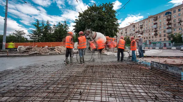 Tramvay rayları onarılan ve bakım süreleri yüksek olan yol inşaatı. Metal bir şebekeye beton dökülüyor. Kavşağın ortası. Arkaplanda yeşil ağaçlar