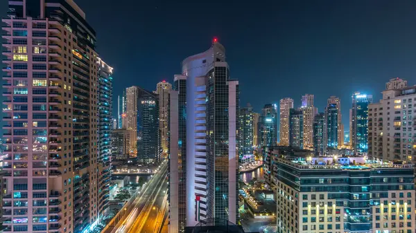 Dubai Marina 'nın hava panoramik görüntüsü gece görüş mesafesinden. Parlayan pencerelerle aydınlatılmış modern gökdelenler ve konut kuleleri. Yolda trafik vardı.