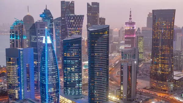Batı Körfezi bölgesinin ufuk çizgisi Doha 'da günden geceye geçiş zamanı, Katar. Günbatımından sonra modern gökdelenlerin çatıdan görünüşü aydınlandı. Yolda trafik vardı.