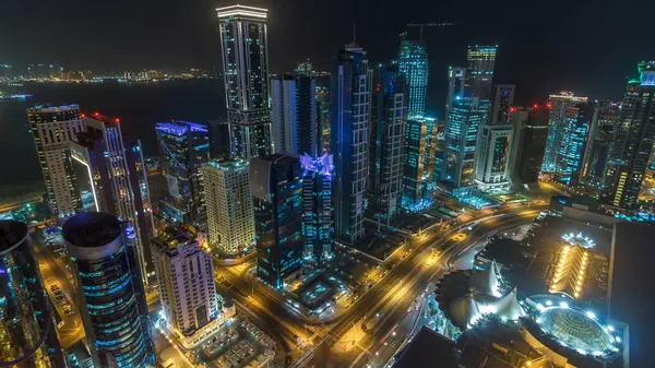 Katar 'ın Doha Zaman Çizelgesi' nde Batı Körfezi bölgesinin ufuk çizgisi. Aydınlatılmış modern gökdelenler geceleri çatıdan gökyüzü manzarası. Yolda trafik vardı.