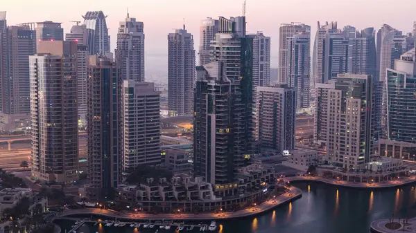 Dubai yat limanı, gece gündüz tekne ve yat panoramasıyla geçiş zamanı, aydınlatma ışıkları kapalı, BAE. Gökdelenleri ve kuleleri olan gökyüzü manzarası