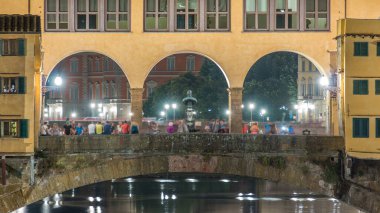 İtalya 'nın Floransa kentindeki Arno nehrinin üzerindeki ünlü Ponte Vecchio köprüsü gece aydınlandı. Manzarayı kapat. Suyun yansıması. Kalabalık ortada yürüyor..