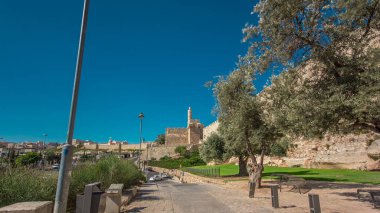 Antik kutsal Kudüs zaman tünelinin savunma duvarı. Parlak güneş tarafından aydınlatılan hiperhız. Harika yeşil çimenler ve mavi gökyüzü. Yolda trafik vardı.